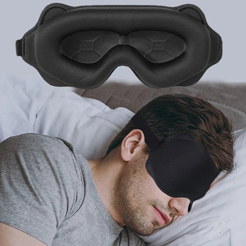 The contoured black sleep mask above a person wearing it lying on a pillow