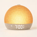 Linen-textured sunrise alarm clock glowing amber on an ivory studio background.