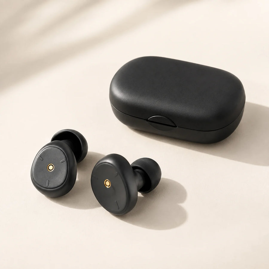 Black silicone earplugs and their carry case on a warm ivory surface.