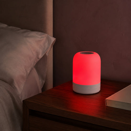 Red-mode lamp on a walnut bedside table beside ivory bedding.